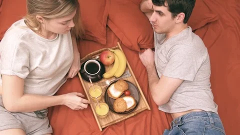 Young couple is lying in bed  and having a healthy breakfast. 動画素材 74076132