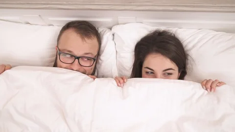 Young couple lying on the bed and looking out of the blanket.  Stock Footage 102399223