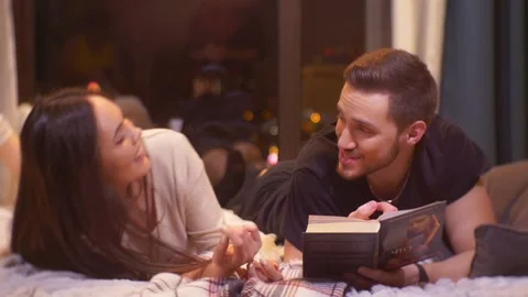 Young Couple is Lying on the bed and Reading a Book Stock Footage 163467192