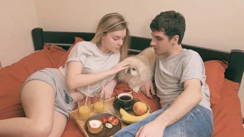 Young couple is lying in bed with dog and having a healthy breakfast. 動画素材 74074932