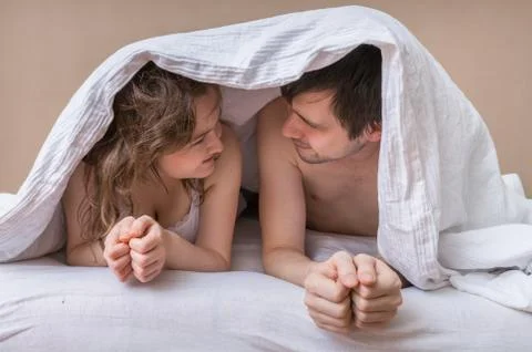 Young couple lying in bed under blanket and looking in their eyes. Foto stock