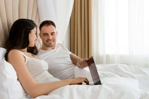Young couple lying in bed using laptop Stock Photos