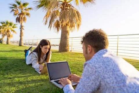 Young couple lying on the grass in smart working with laptop facing each othe Stock Photos