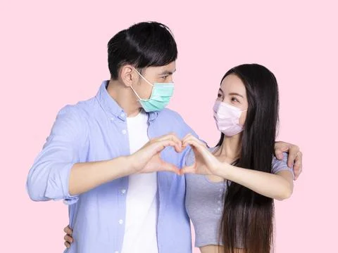 Young couple making hand heart gesture and wearing medical mask Stock Photos