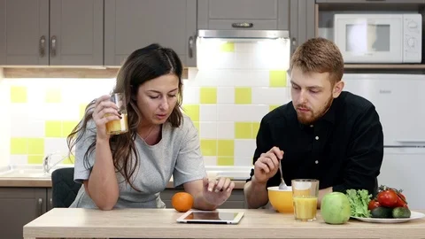 Young couple man and woman with tablet eating breakfast sitting by table in Vidéo 103940407