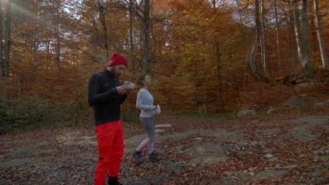 Young couple with maps in their hands running in autumn forest. Stopped to check Video stock 166159176