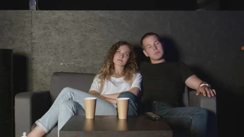 A young couple of millennials sits on the couch in front of the TV Stock Footage 136344178