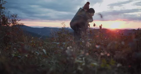 Young couple in a mountain top field, playing and watching a beautiful sunset Stock Footage 141018707