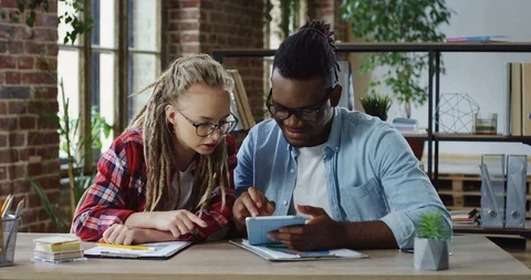 Young couple of multiethnical hipsters with dreadlocks sitting at the table and Stock Footage 101002078