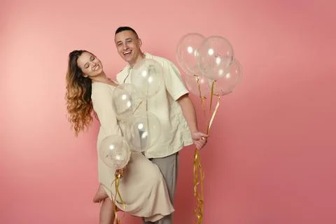 A young couple in pastel clothes, balloons on a pink background. Lovers cel.. Stock Photos