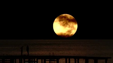 Young couple on pier set against timelapse full moon Stock Footage 1036113