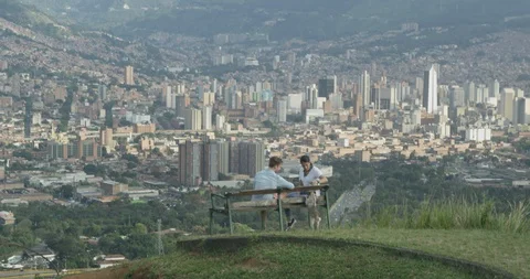 Young couple playing with dog and talking on park bench overlooking city skyline Stock Footage 86150112