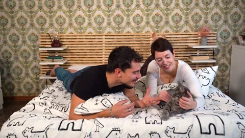 Young couple is playing with their cat on the bed. Video stock 229556063