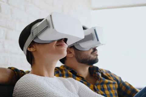 Young Couple Playing Virtual Reality With Headset On Sofa Stock Photos
