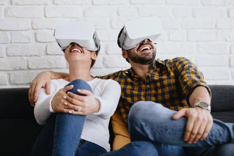 Young Couple Playing Virtual Reality With Headset On Sofa Stock Photos