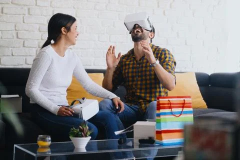 Young Couple Playing Virtual Reality With Headset On Sofa Stock Photos