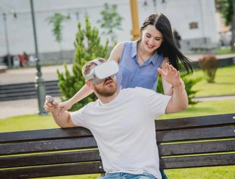 A young couple plays a game using virtual reality glasses on the street. Stock Photos