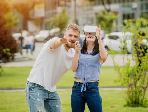 A young couple plays a game using virtual reality glasses on the street. Stock Photos