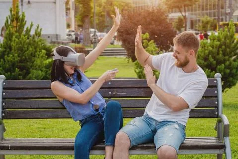 A young couple plays a game using virtual reality glasses on the street. Stock Photos