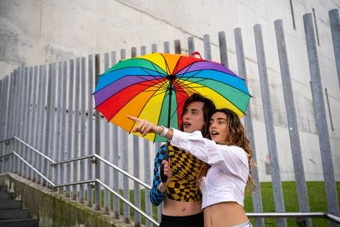 Young couple pointing at a point in amazement while holding an umbrella with gay Stock Photos