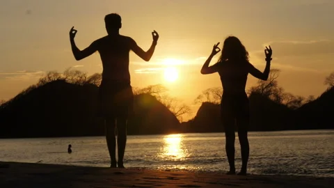 Young couple practicing yoga on the beach at sunset Stock Footage 106939229