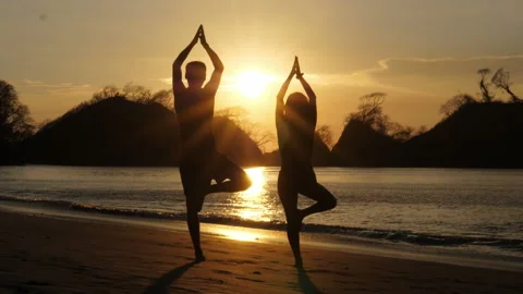 Young couple practicing yoga on the beach at sunset Stock Footage 106939394
