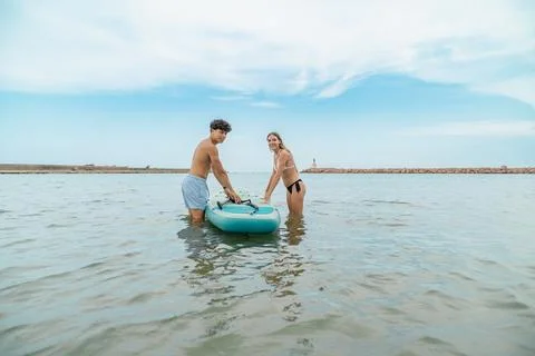Young couple preparing inflatable sup board in the sea Stock Photos