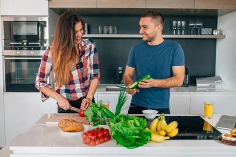Young couple preparing salad in the kitchen. They are cutting tomatoes and cu Stock Photos