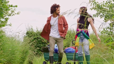 Young Couple Pulling Trolley Filled With Camping Equipment Through Field To Stock Footage 312694559