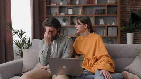 Young couple quarreling while using laptop while sitting on sofa at home. Young Stock Footage 195015367