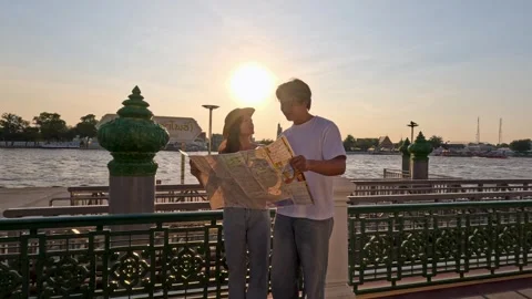 Young couple reading city map by riverside at sunset Stock Footage 324700378