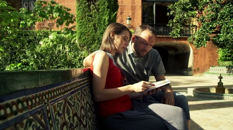 Young couple reading guide book sitting in garden in Seville, Spain HD Stock Footage 48496409