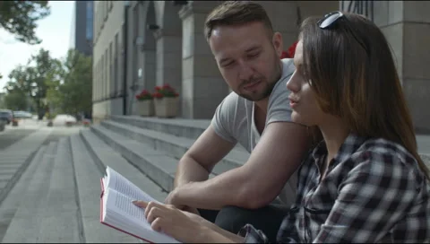 Young couple reading together while sitting on university stairs, outdoors. Stock Footage 54416325