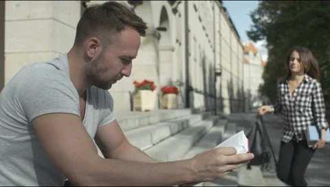 Young couple reading together while sitting in front on stairs, outdoors. Stock Footage 54418642