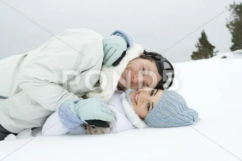 Young Couple Reclining Together In Snow, Smiling, Portrait