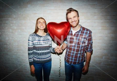 Young couple with red heart-shaped balloon looking at camera Stock Photos