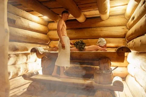 Young couple relaxing and sweating in hot sauna wrapped in towel. Woman, man Stock-Fotos