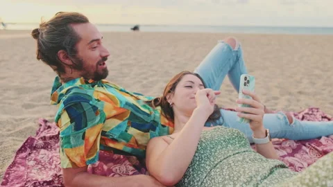 Young couple relaxing on the beach, talking, using mobile phone Stock Footage 227143937