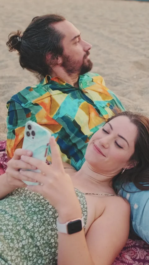 Young couple relaxing on the beach. Young woman using mobile phone Stock Footage 227136357