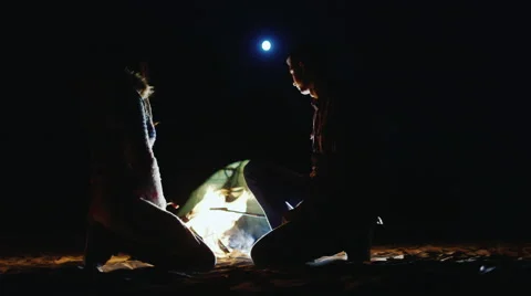 Young couple relaxing by the fire, roasting sausages over a fire. In the sky the Stock Footage
