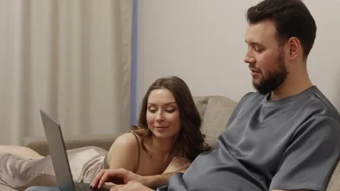 Young Couple Relaxing on Sofa Browsing Internet on Laptop Stock Footage 304983352