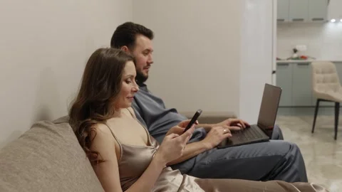 Young Couple Relaxing on Sofa Using Laptop and Smartphone Stock Footage 304983187