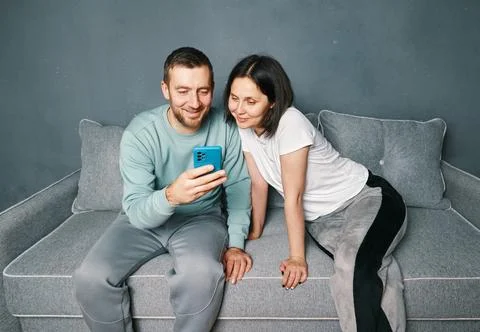 Young couple relaxing on sofa using mobile smart phone relaxing at home Stock Photos