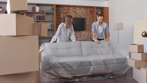 Young couple removing the protective cover from the sofa in new apartment on Stock Footage 268763074