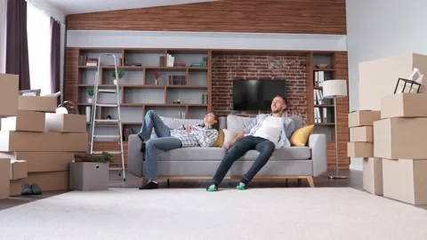 Young couple resting on sofa between cardboard boxes in new apartment on moving 스톡 동영상 237463564