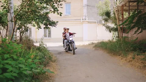 Young couple riding a motorcycle through a scenic pathway surrounded by greenery Stock Footage 313847355