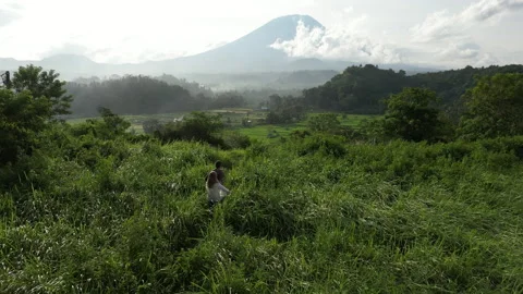 Young couple run into high grass, mountain volcano Agung on background Stock Footage 270272283