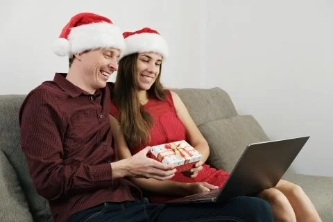 Young Couple in Santa Hat Using a Laptop for Video Call and Holding Gift Box. Stock Photos
