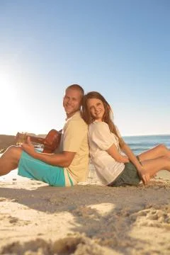 Young couple sat back to back on the beach 스톡 사진