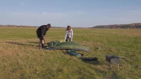 Young couple setting up a tent in a large green meadow Stock-Footage 319792250